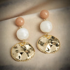 Pair of earrings with gold discs, white beads, and pink beads on a beige fabric background