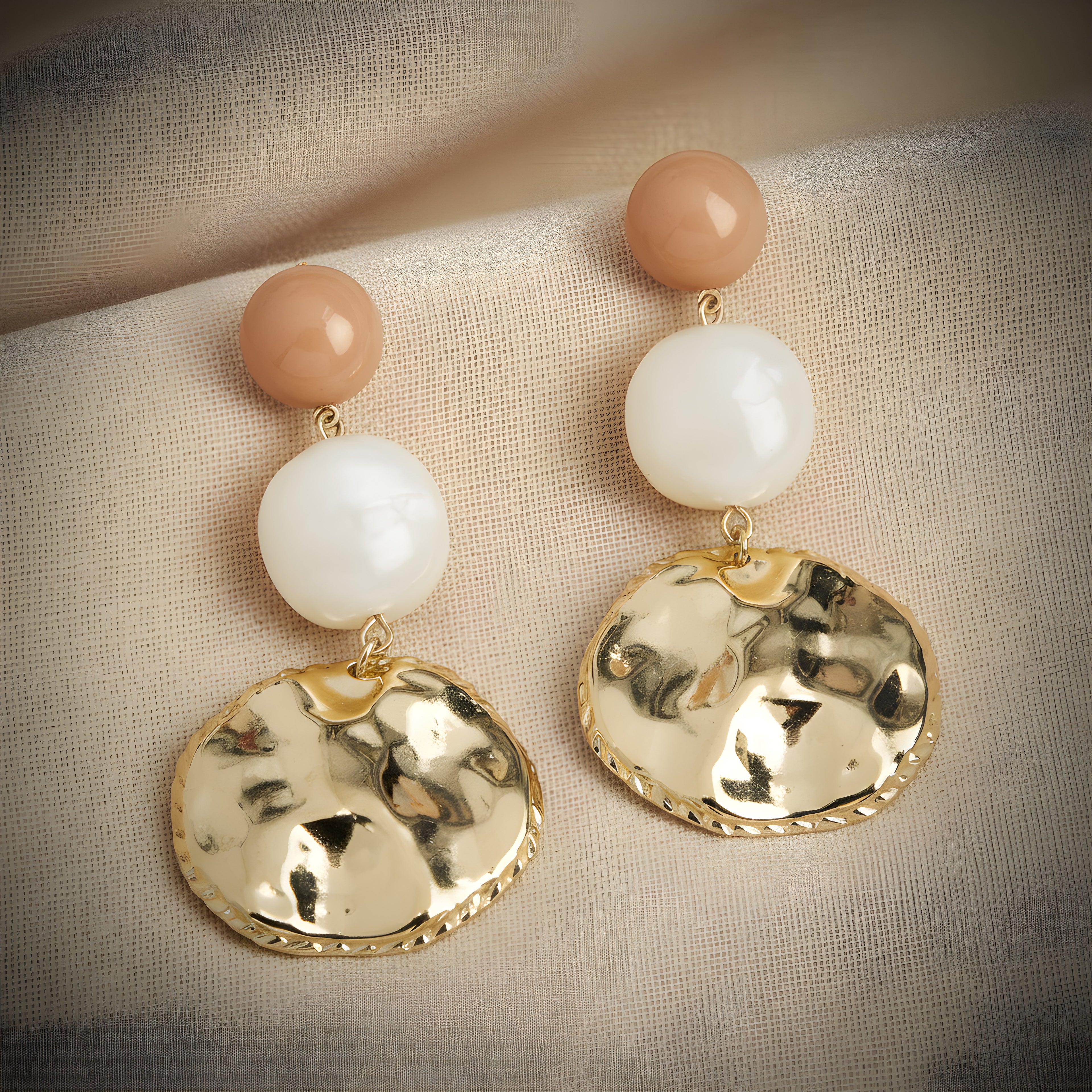 Pair of earrings with gold discs, white beads, and pink beads on a beige fabric background